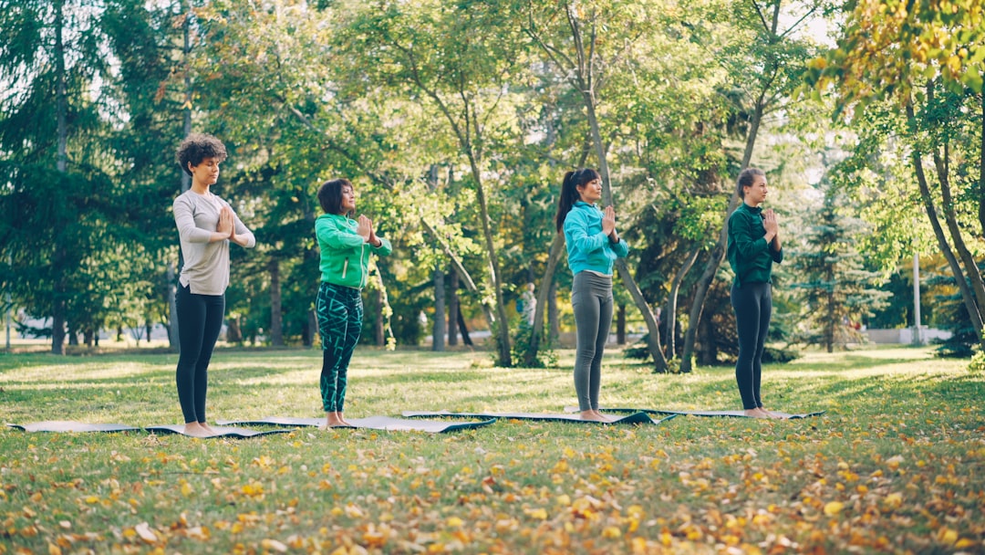 Flexible young ladies are doing yoga exercises then relaxing and breathing standing on mats in park on autumn day. Healthy lifestyle, active people and nature concept.